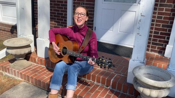 A musician sitting on a porch with a guitar across their lap.