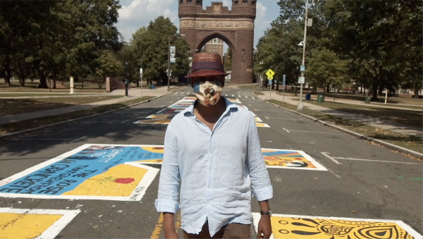 A Black man wearing a mask and walking down a street covered in murals. 