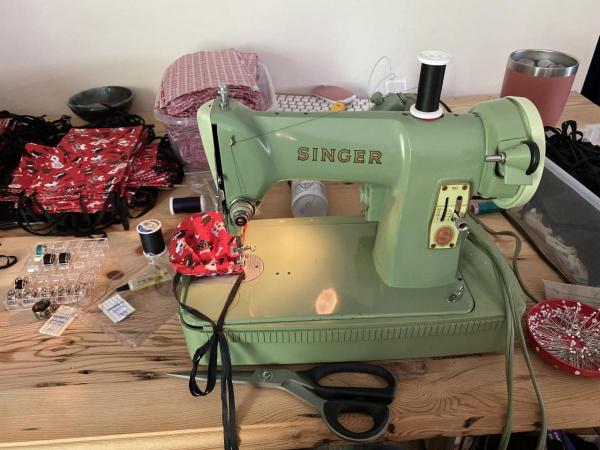 An old, green Singer sewing machine being used to make masks.