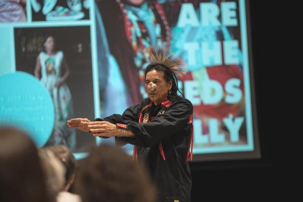 Tchin Storytelling while wearing Indigenous clothing and wearing a bunny snout mask