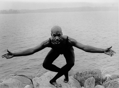renowned dancer, choreographer, and civil rights activist Arthur Hall doing a plie in a black leotard and tights. He stands on a rock at the edge of a body of water