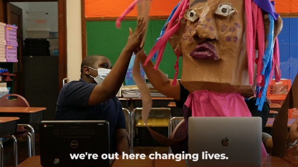 A masked boy at school high-fives one of the SpiralQ puppets. They are both sitting in front of laptops, and a caption reads: we're out here changing lives.