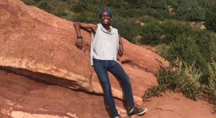 B.J. posing on a hill of orange rock. They are wearing a white top, jeans and a huge smile!